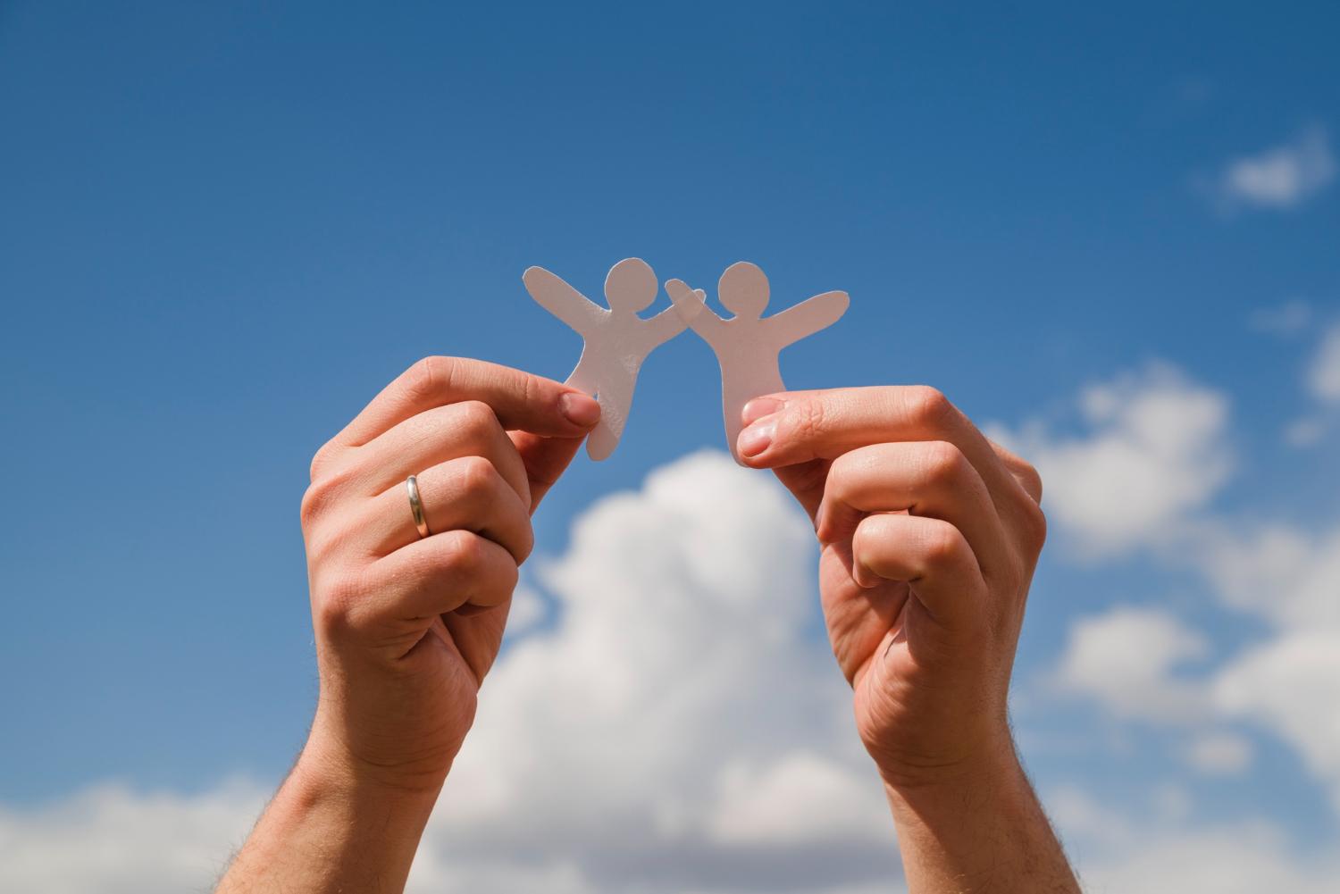 Dos manos sosteniendo figuras de dos personas tomadas de la mano.